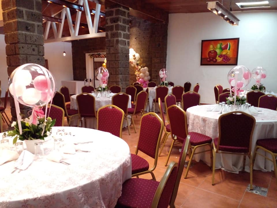 Salón montado en vino tinto y dorado con centros de mesa de globos rosados